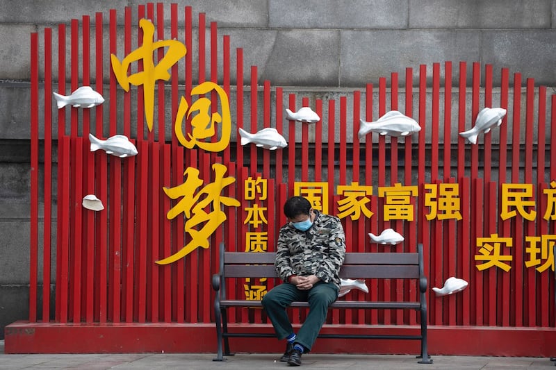 湖北武汉一名居民2020年4月1日在“中国梦”宣传标语前打盹( 美联社)