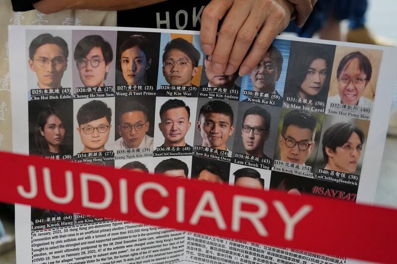 2021年7月8日,一名支持者在香港法院外举着标语牌声援47名民主被告的照片。(美联社)