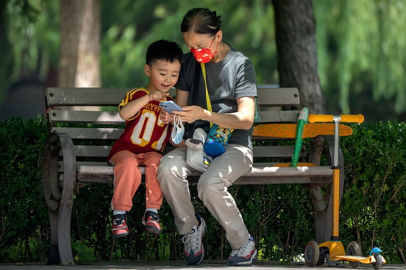 一名妇女和一个孩子坐在北京一座公园的长凳上看手机(美联社)